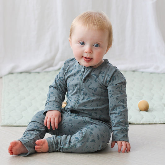 Baby boy sitting on wooden floor posing in Marks Long Sleeve Zip Suit, designed by Burrow and Be