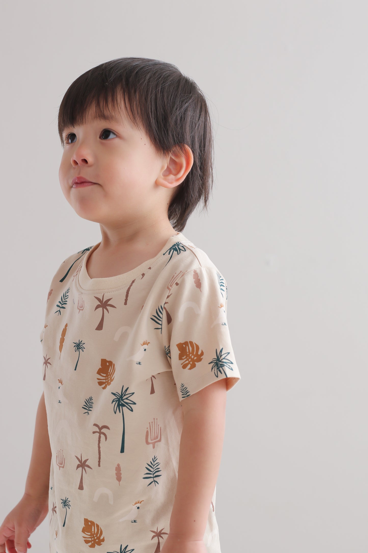 Boy standing against a white wall while wearing a Jungle Stamp Classic T-Shirt, designed by Burrow and Be