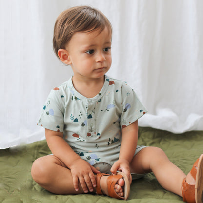 Baby sitting on floor while wearing Garden Treasure Alex Romper from Burrow and Be and sandals from Wanders