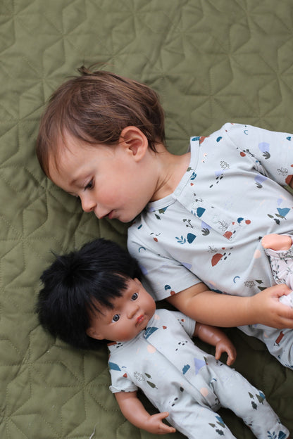 Baby lying on the ground wearing Garden Treasure Alex Romper from Burrow and Be beside doll wearing garden treasure onesie for dolls