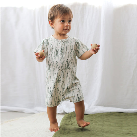 Baby boy wearing String of Pearls Alex Romper from Burrow and Be and holding two balls while walking