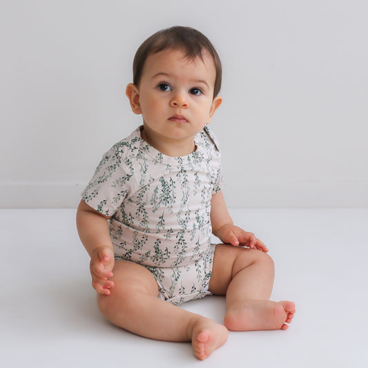 Baby sitting on white floor in front of a white wall while wearing String of Pearls Short Sleeve Bodysuit, designed by Burrow and Be