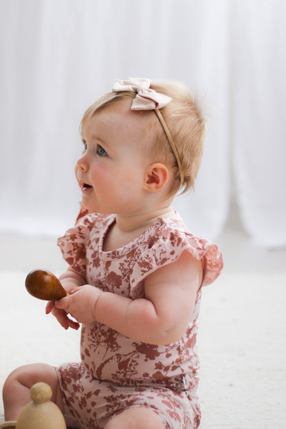 Toddler wearing Burrow and Be Flower Splash Flutter Bodysuit and playing a wooden shaker