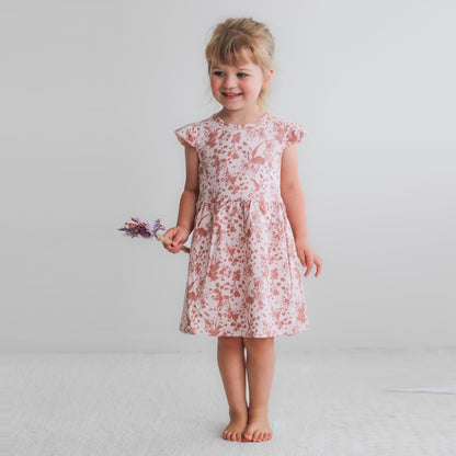 Girl model posing for camera against a white background while wearing Flower Splash Flutter Dress, designed by Burrow and Be