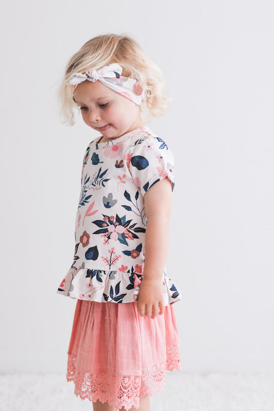 Girl standing in front of a white wall while wearing Pink Clementine Headband and Hana Top with a Blush Skirt, all designed by Burrow and Be