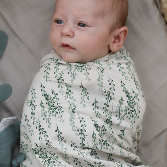 Baby laying on Essential Muslin Wrap in Sage while wrapped in String of Pearls Muslin Wrap, both designed by Burrow and Be