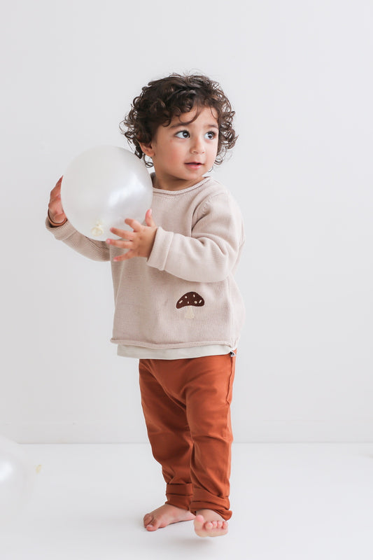 Boy holding a balloon standing in front of a white background, wearing Marley Pants - Chestnut, designed by Burrow and Be