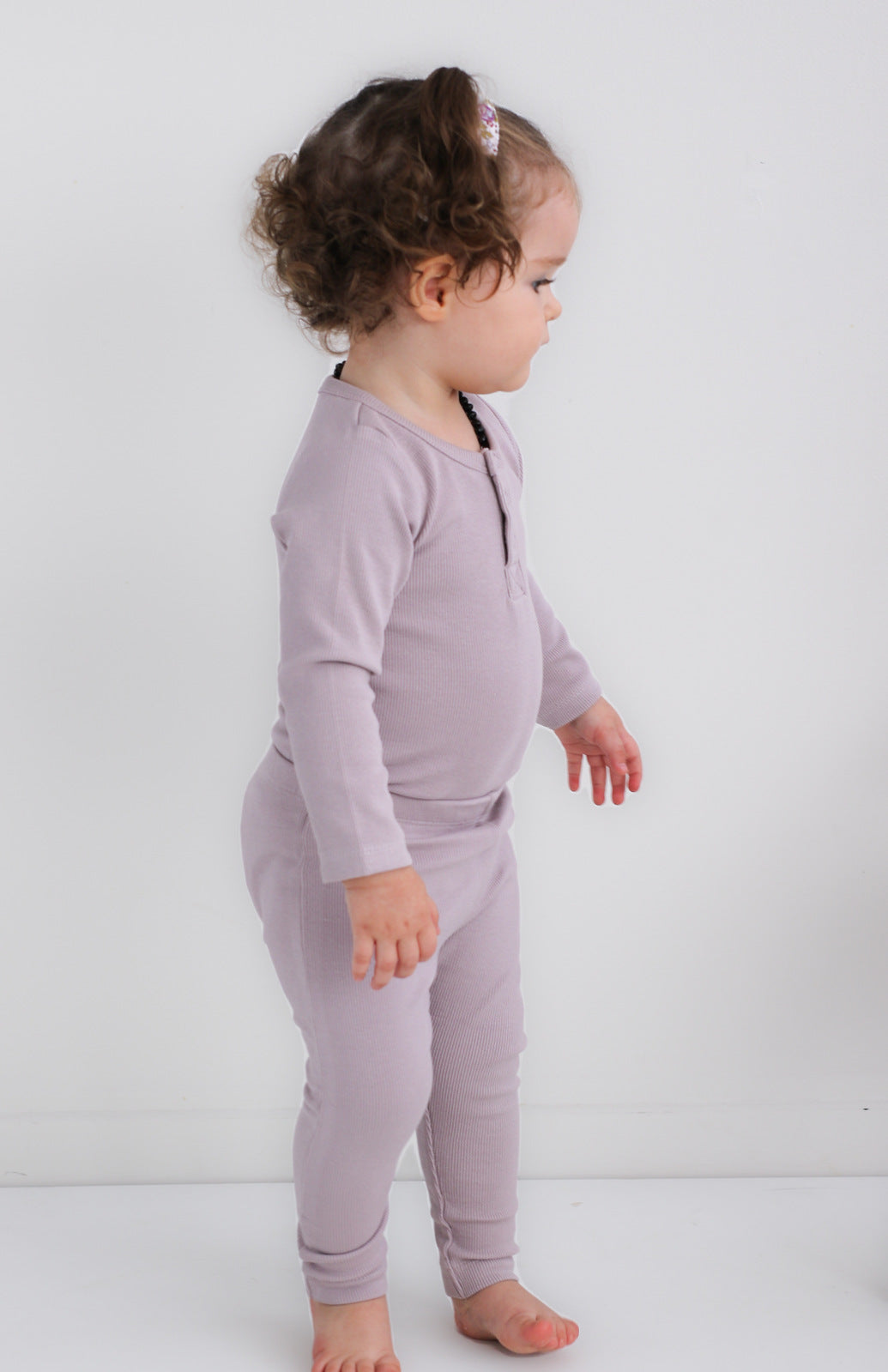 Girl standing against white background wearing Long Sleeve Bodysuit and Essential Derby Rib Leggings - both in Lavender and designed by Burrow and Be