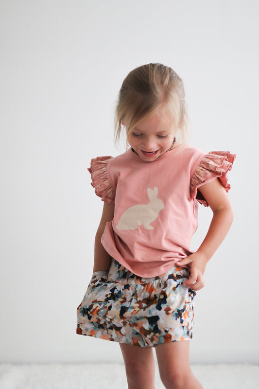 Girl smiling and looking down while wearing Doe Flutter T-shirt and Delight Lyla Shorts by Burrow and Be