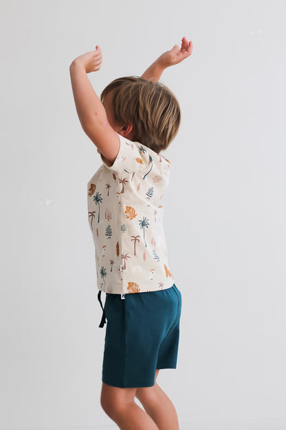 Boy jumping towards a white background while wearing a Jungle Stamp Classic T-Shirt and Leo Shorts in Deep Teal, both designed by Burrow and Be