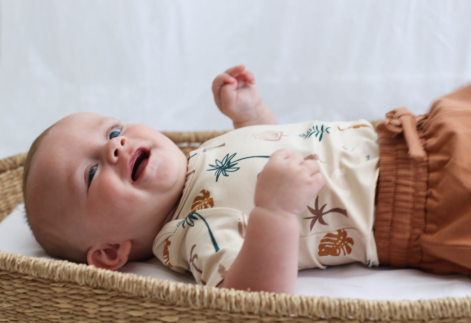 Baby staring at camera while laying in Moses Basket and wearing Leo Shorts in Tan and Jungle Stamp Bodysuit, all designed by Burrow and Be