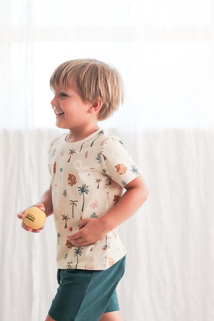 Boy holding a ball running against a white curtain while wearing Leo Shorts in Deep Teal and Jungle Stamp Classic T-Shirt, all designed by Burrow and Be