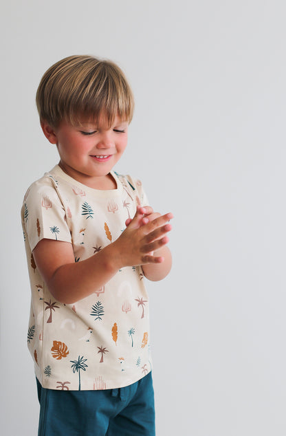 Boy standing against a white wall while wearing Leo Shorts in Deep Teal and Jungle Stamp Classic T-Shirt, all designed by Burrow and Be