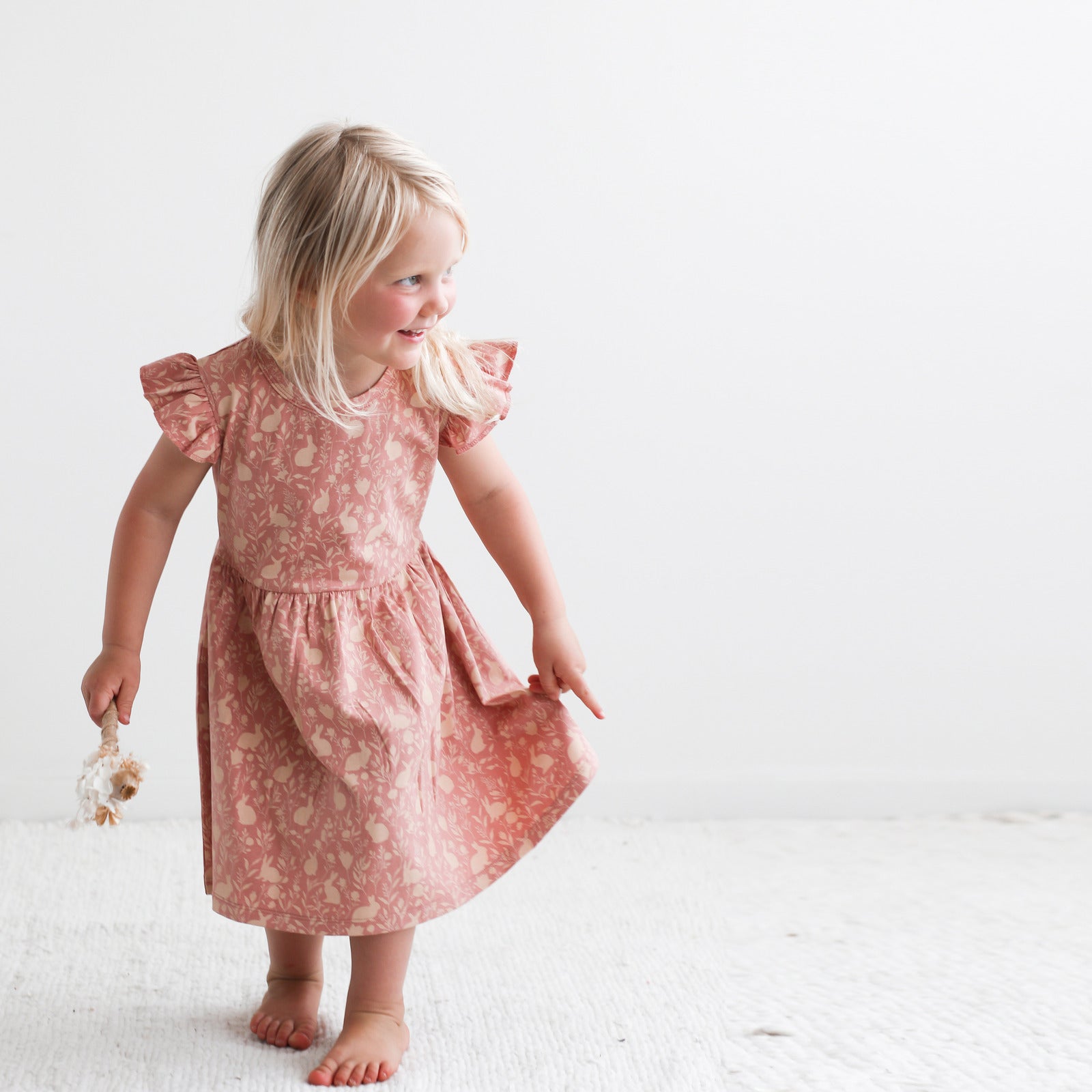 Girl wearing Mead-Doe Flutter Dress designed by Burrow and Be while walking on white carpet, in front of a white wall.