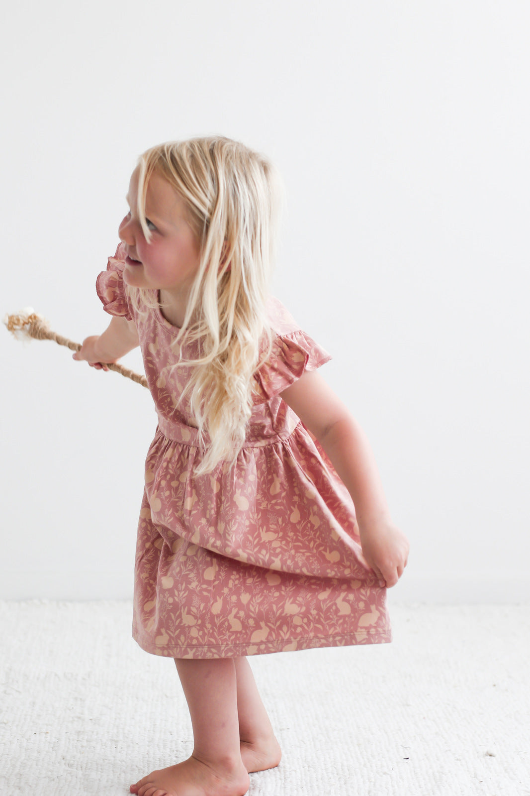 Girl wearing Mead-Doe Flutter Dress designed by Burrow and Be while posing on white carpet, in front of a white wall.