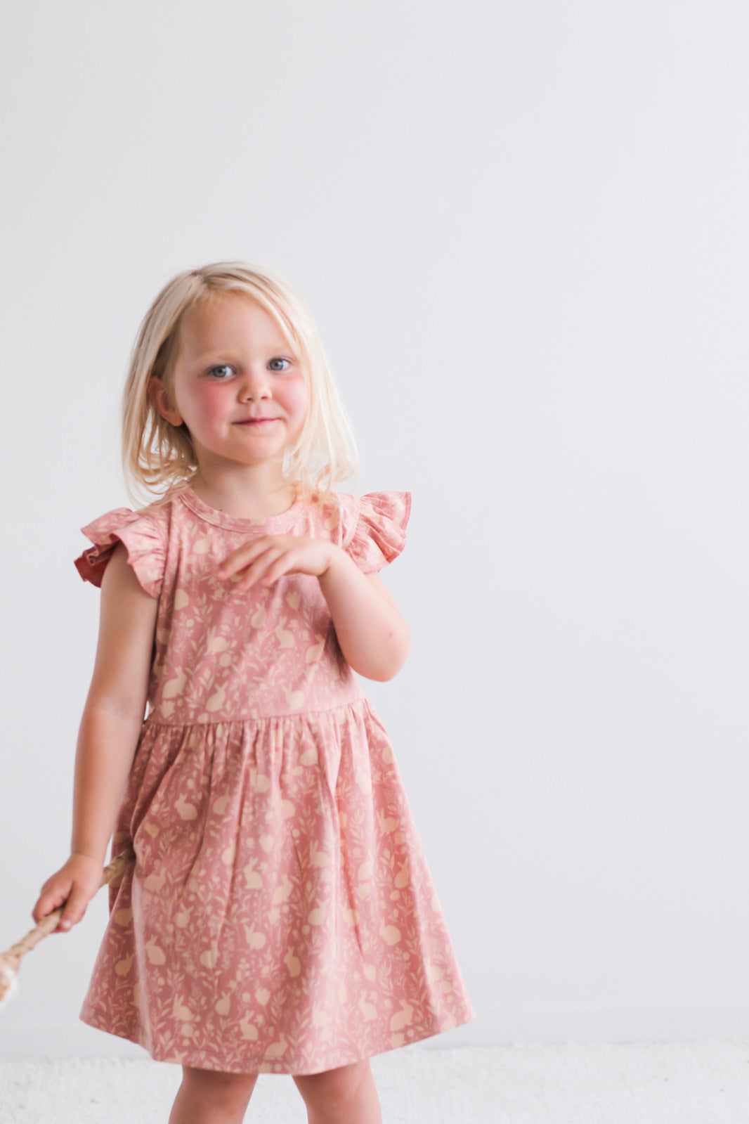 Girl posing in front of a white wall while wearing Mead-Doe Flutter Dress, designed by Burrow and Be 