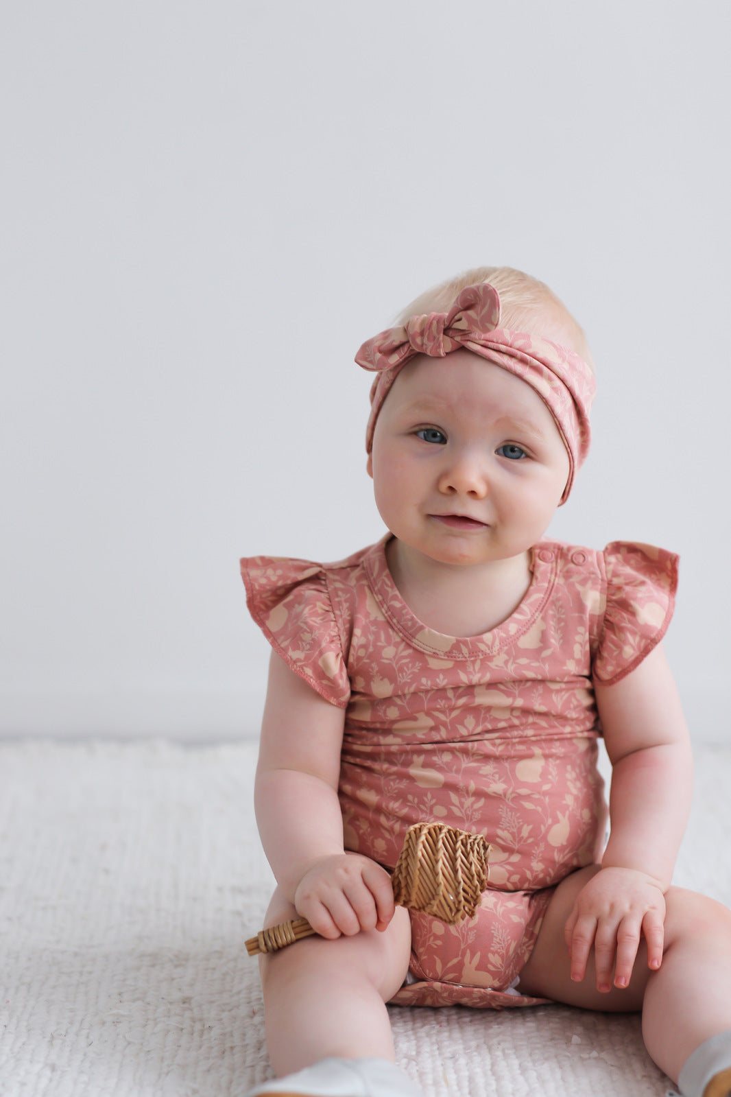 Baby girl posing at camera while wearing Flutter Bodysuit and Essential Baby Headband both in Mead-Doe print, designed by Burrow and Be