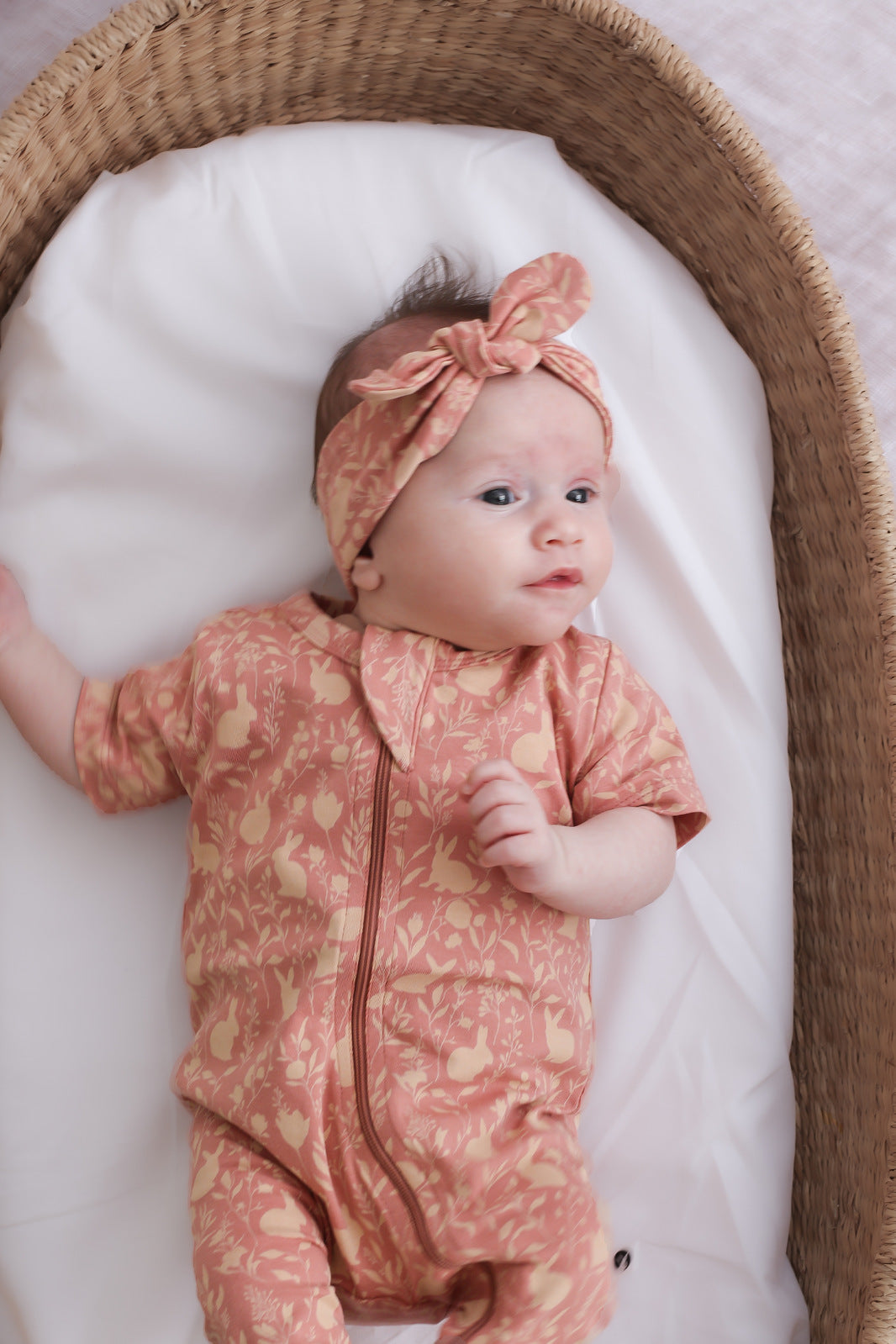 Baby girl laying in moses basket and wearing Short Sleeve Zip Suit and Essential Baby Headband both in Mead-Doe print, designed by Burrow and Be