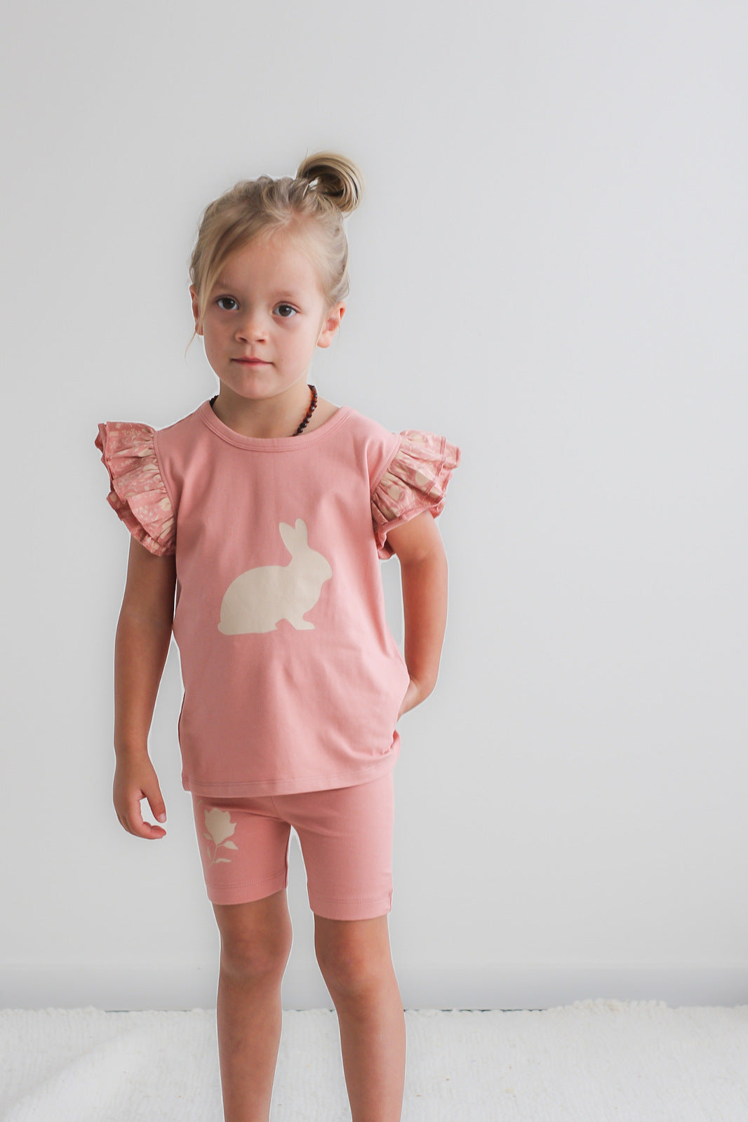 Girl standing in front of white background, wearing Doe Flutter T-Shirt and Mead Bike Shorts, both designed by Burrow and Be