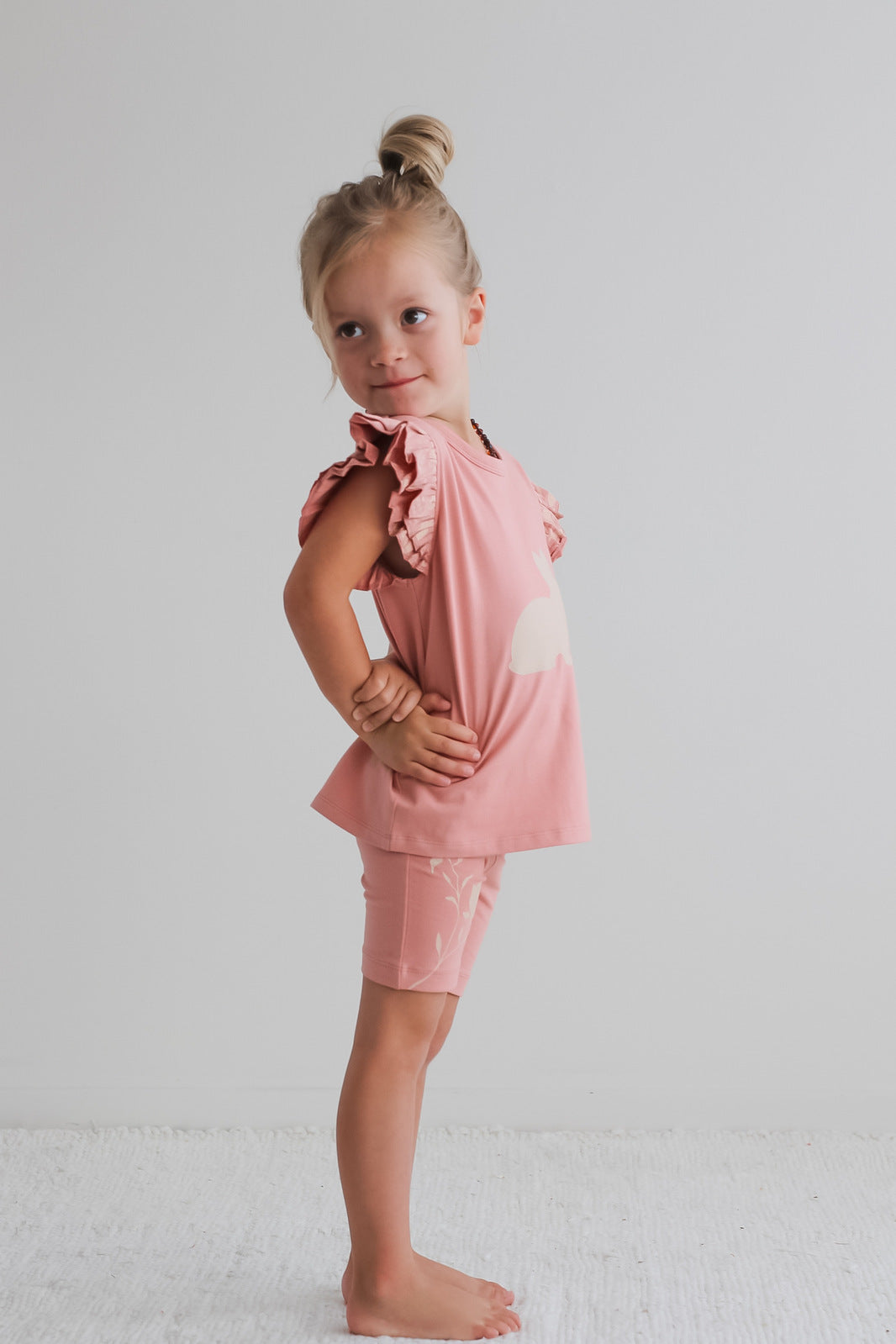 Girl standing in front of white background, posing facing right while wearing Doe Flutter T-Shirt and Mead Bike Shorts, both designed by Burrow and Be