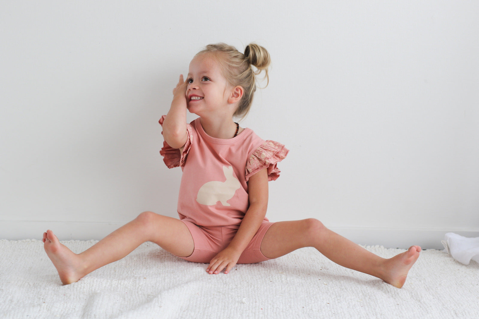 Girl sitting on carpet in front of white background, posing at the camera while wearing Doe Flutter T-Shirt and Mead Bike Shorts, both designed by Burrow and Be