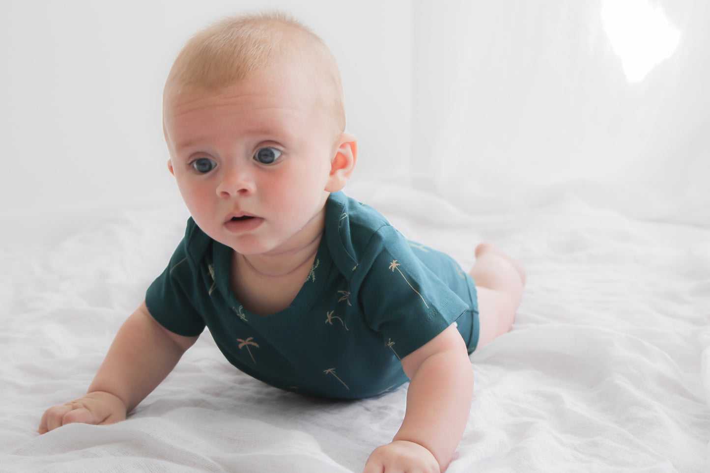 Baby laying on white sheets while wearing Palm T-shirt Bodysuit, designed by Burrow and Be