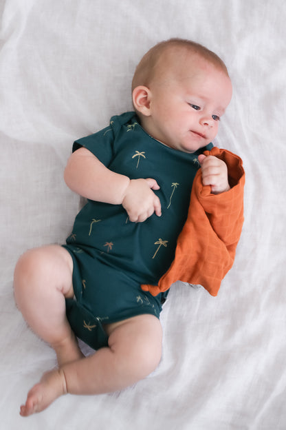 Baby laying on white linen sheets wearing Palm T-shirt Bodysuit, designed by Burrow and Be