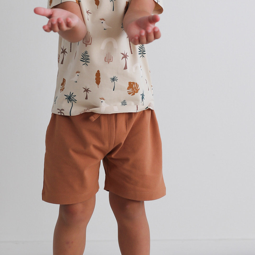 Boy wearing Jungle Stamp Classic T-Shirt and Leo Shorts in Tan, both designed by Burrow and Be, against a white background