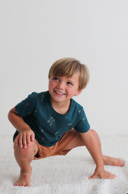 Boy posing against a white background and standing on a white carpet, wearing Palm Classic T-shirt and Leo Shorts in Tan, both designed by Burrow and Be