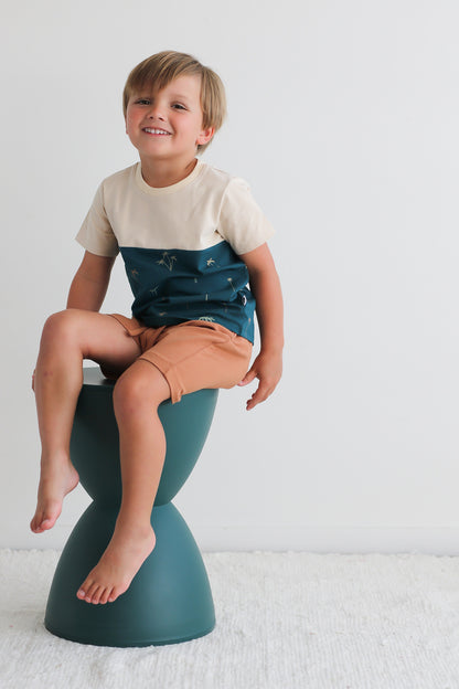 Boy sitting on stool against a white background, wearing Palm Block T-shirt and Leo Shorts in Tan, both designed by Burrow and Be