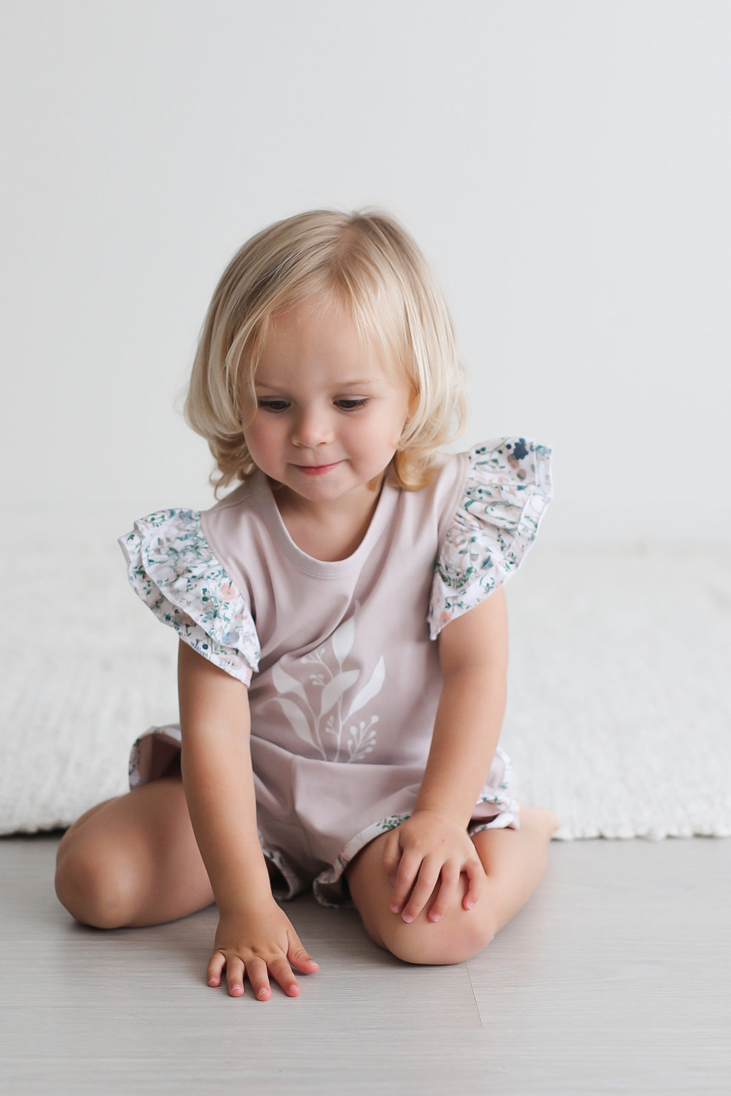 Girl sitting on floor in front of carpet while wearing Wildflower/Lavender Flutter T-Shirt and Penny Shorts, both designed by Burrow and Be