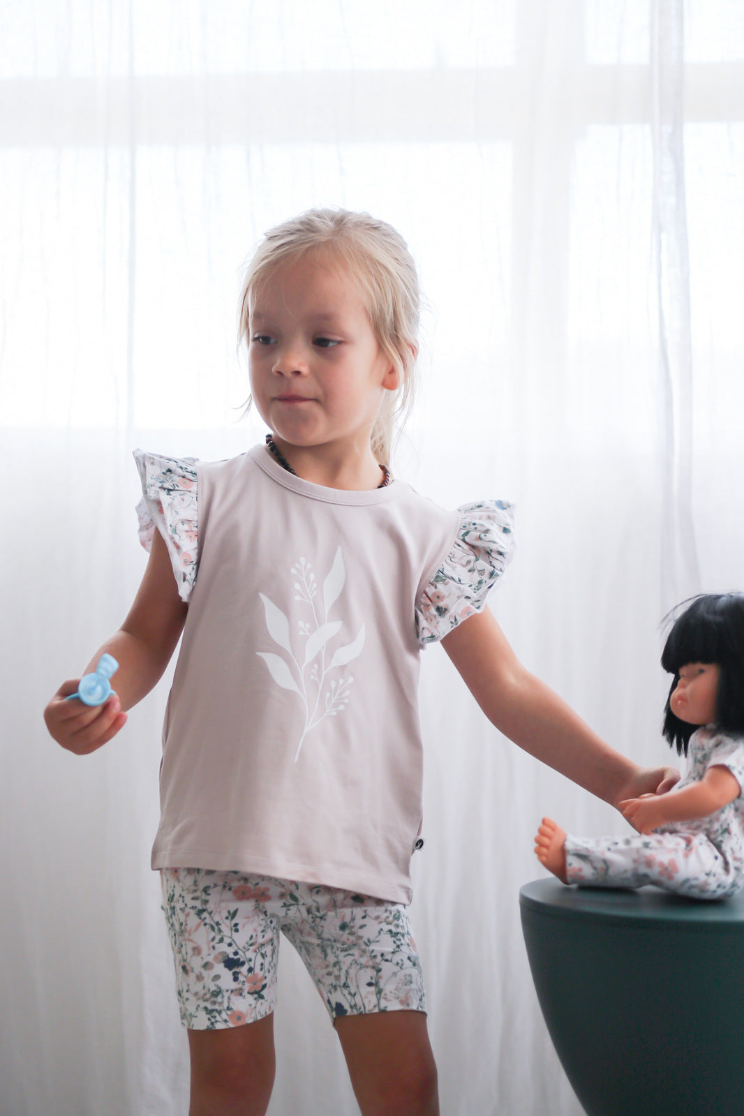 Girl standing in front of white curtains while wearing Wildflower/Lavender Flutter T-Shirt and Wildflower Bike Shorts, both designed by Burrow and Be