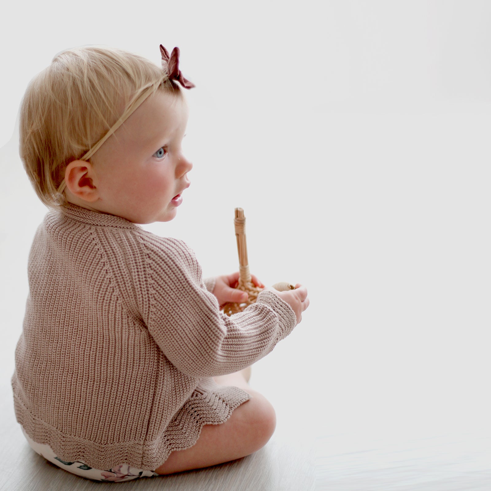 Baby girl back facing the camera while wearing Bow Tie hair band and Florence Knit Cardigan, both designed by Burrow and Be