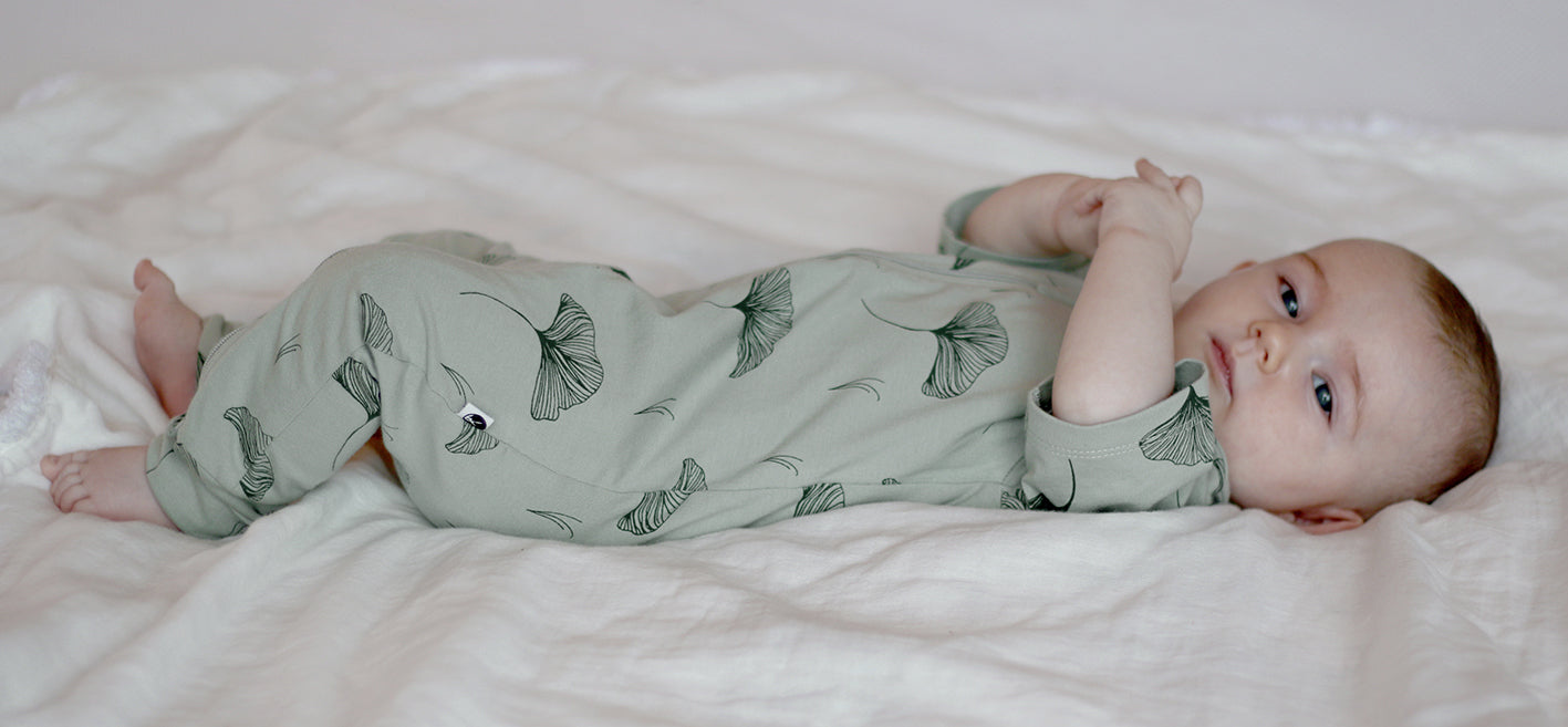 Baby wearing Burrow and Be Ginkgo short sleeve zip suit lying on bed